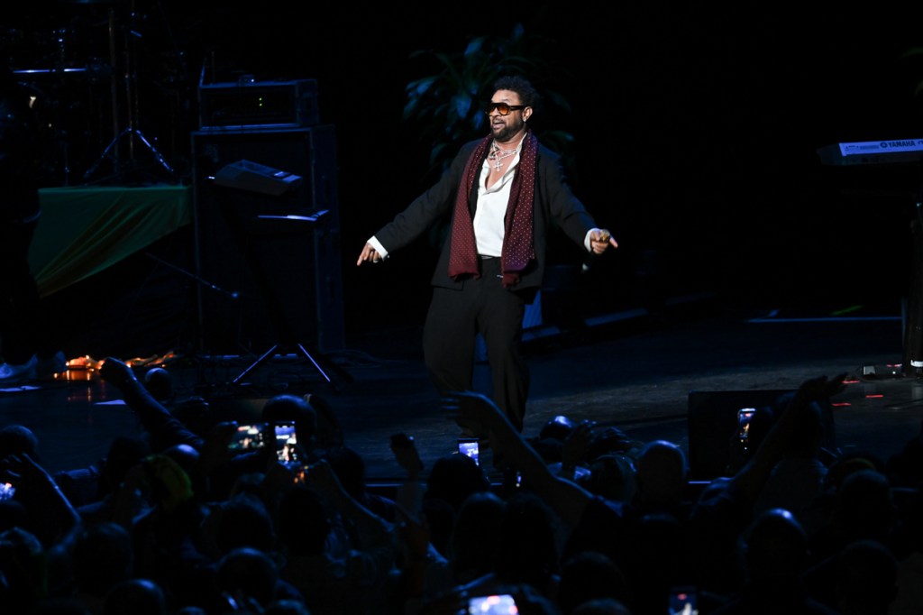 A man wearing black pants and a black jacket singing on stage