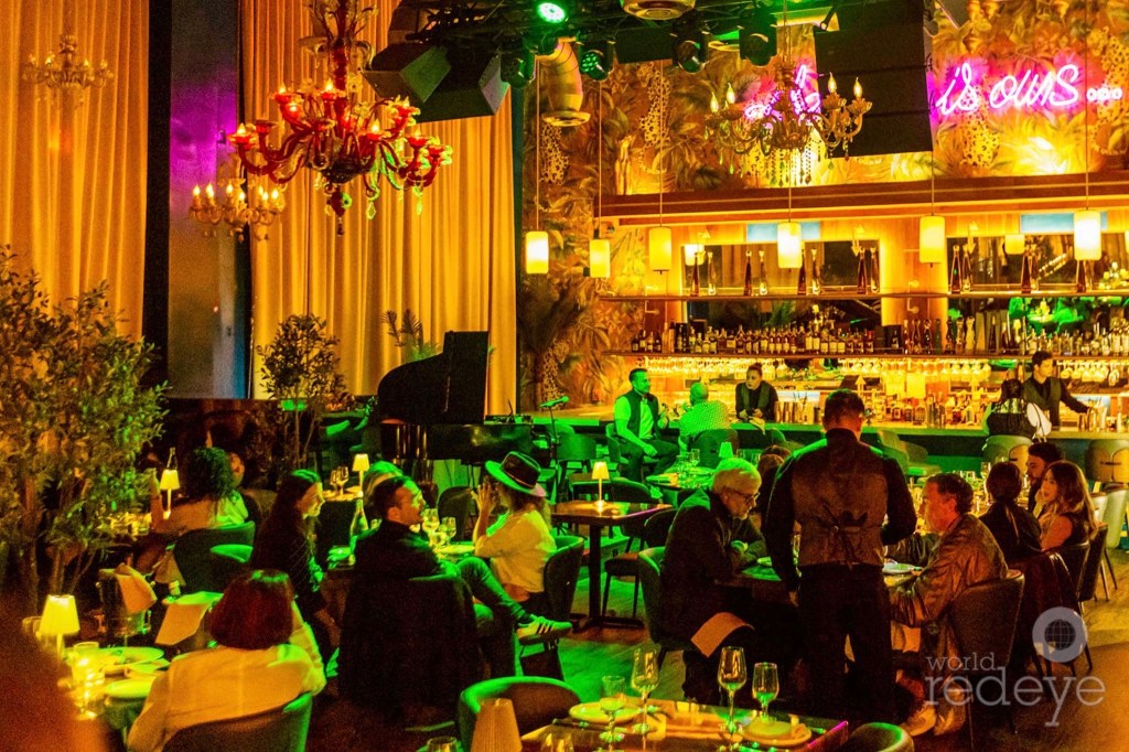 photo of a glamorous dining room bathed in golden and green light with diners, bartenders, and servers