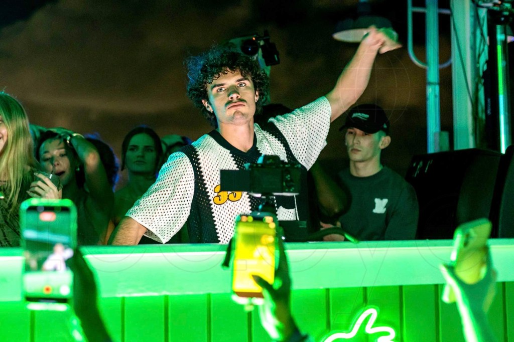 photo of Nick Vans performing in front of a DJ booth glowing in green light as fans record on cell phones