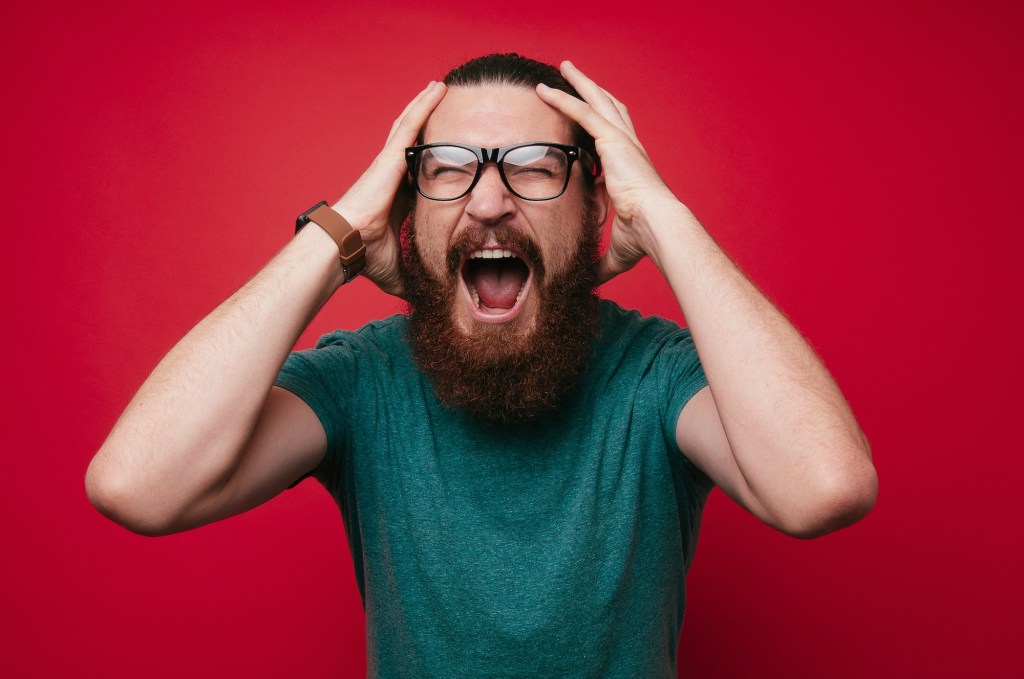 photo of a screaming bearded man looking at the camera with hands on his head