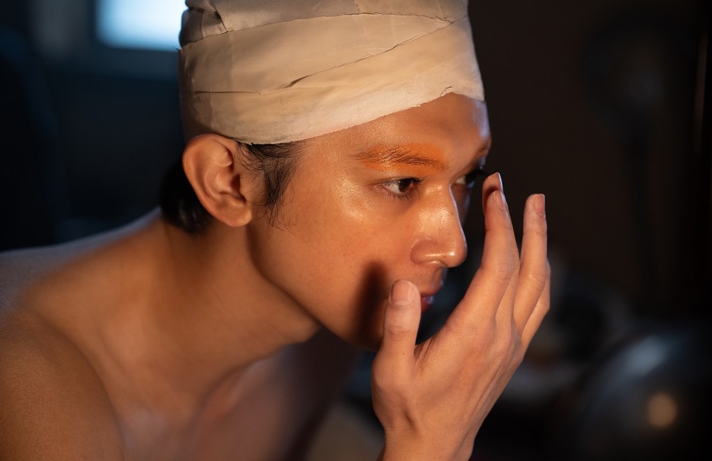 film still of a person applying makeup in front of a mirror