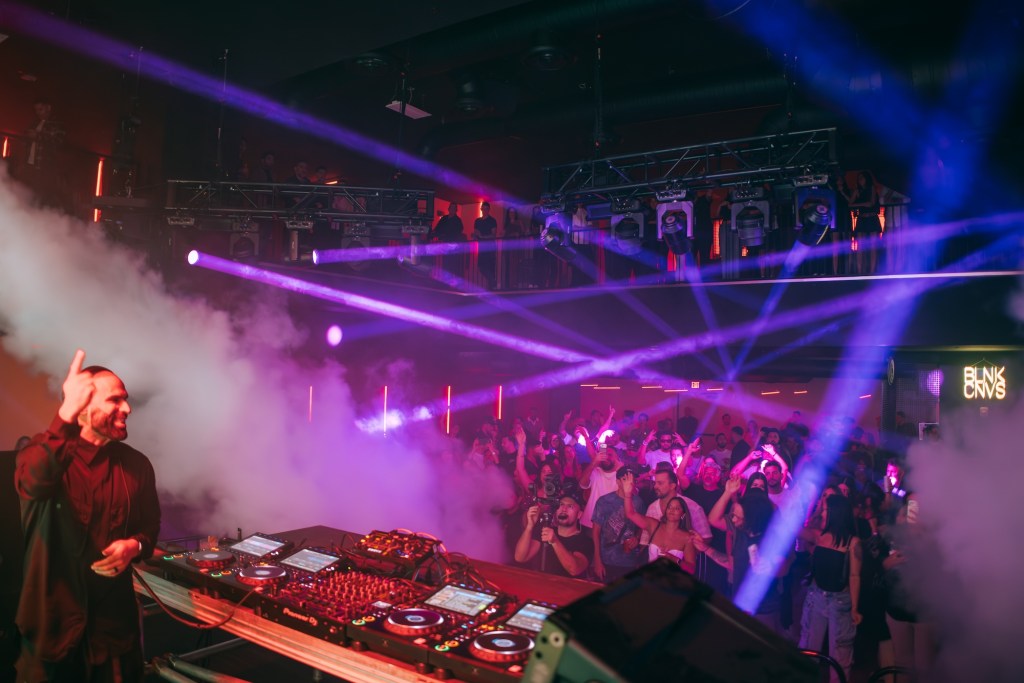 Photo of a DJ on stage in front of a dancing crowd. 