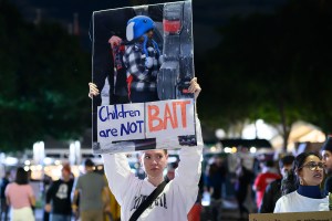 photo of a protester holding sign with a photo of a toddler and text reading, "children are not bait"