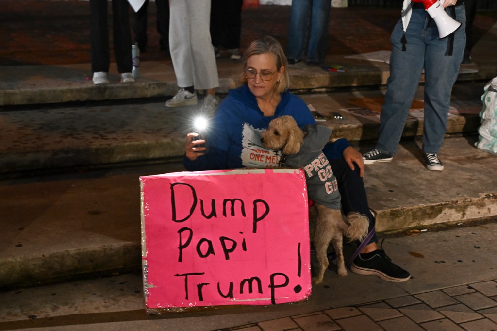 photo of a woman holding a dog in front of a pink sig reading "Dump Papi Trump"
