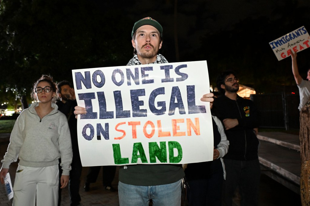 photo of a protester holding a sign reading, "no one is illegal on stolen land"