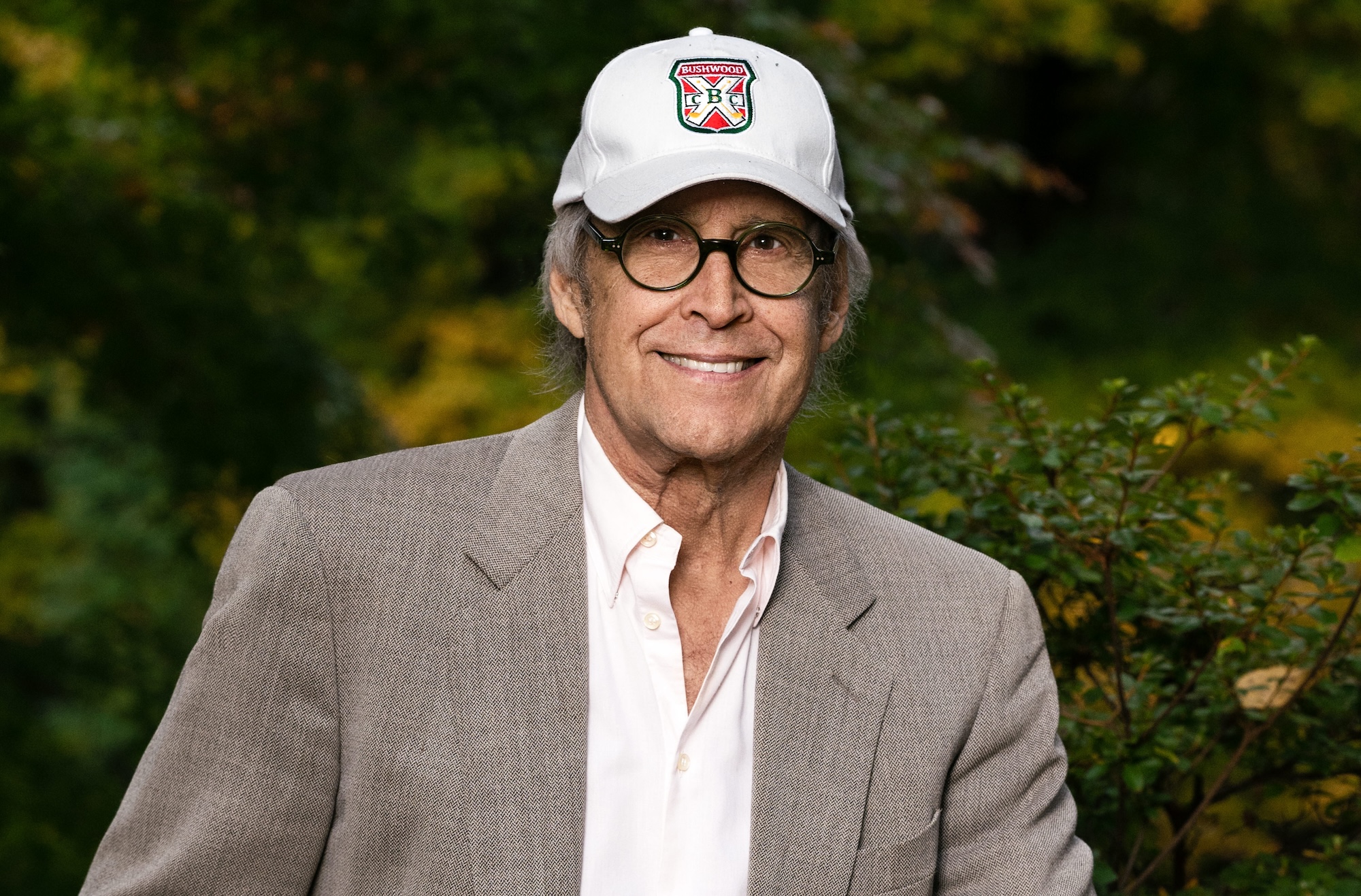 photo of comedian Chevy Chase wearing a baseball cap, white button-down, and blazer