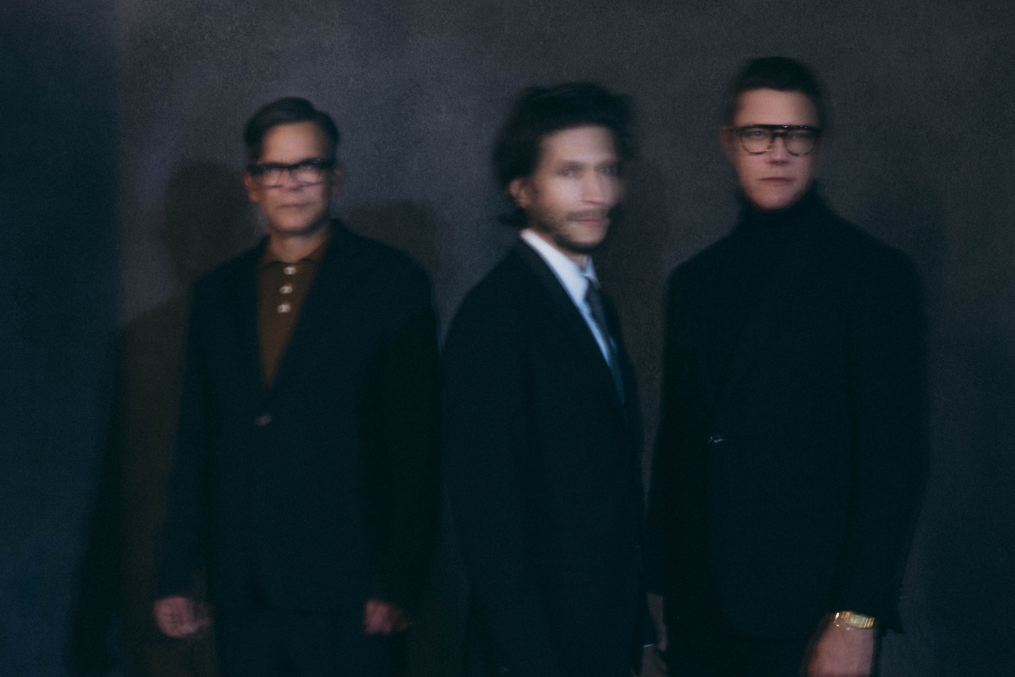 Photo of the three members of the band Interpol in suits. The image is overlayed with a blurry effect