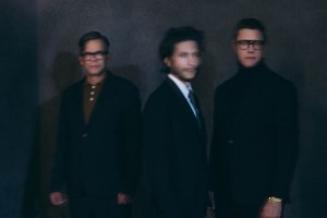 Photo of the three members of the band Interpol in suits. The image is overlayed with a blurry effect