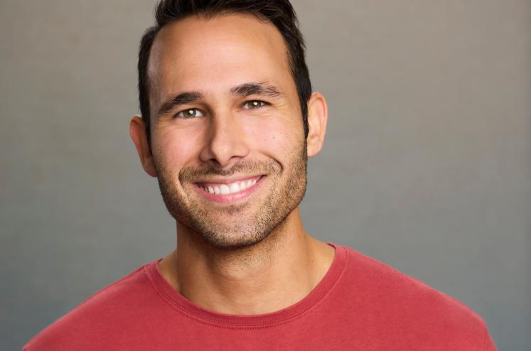 headshot of a smiling man wearing a red shirt in front of a gray background