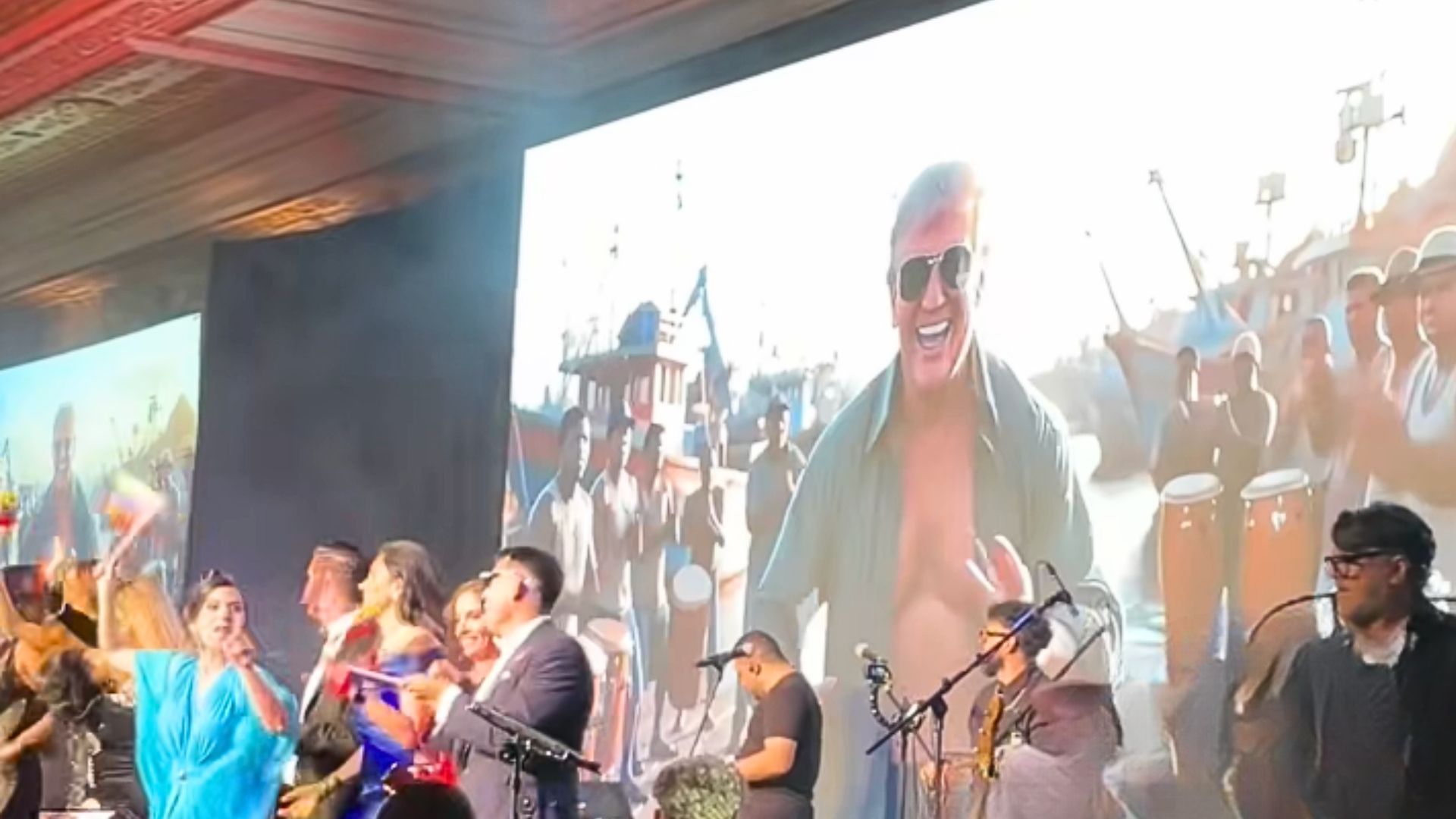 Image of a party with a screen showing an AI generated video of Donald Trump dancing