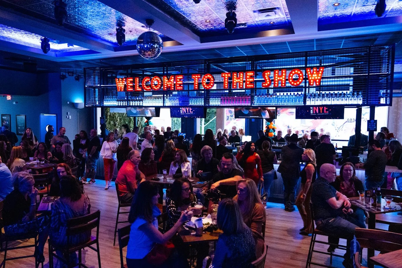 a packed bar with blue lighting and a neon sign