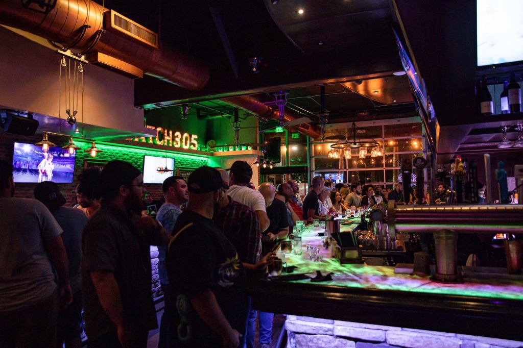 a moody bar with neon lights and people mingling around the large bar