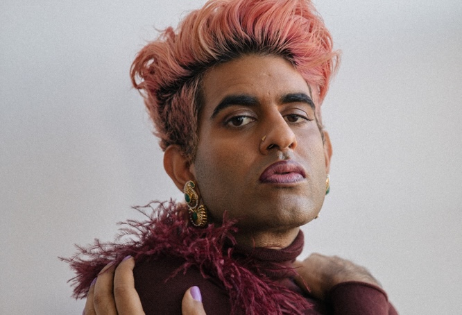 headshot of a person with pink hair and maroon feathered blouse