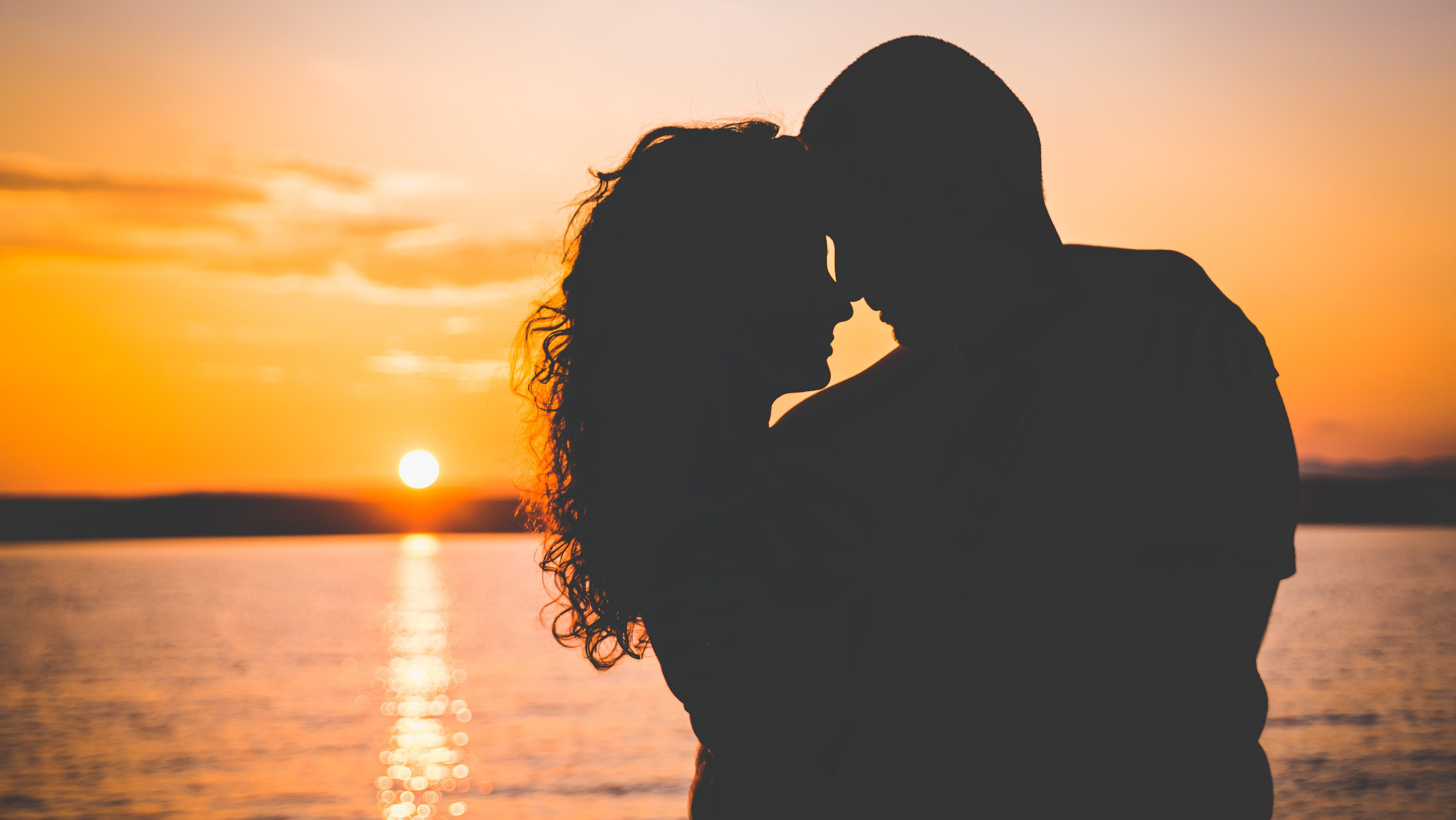 photo of a couple in shadow embracing with the beach behind them at sunset