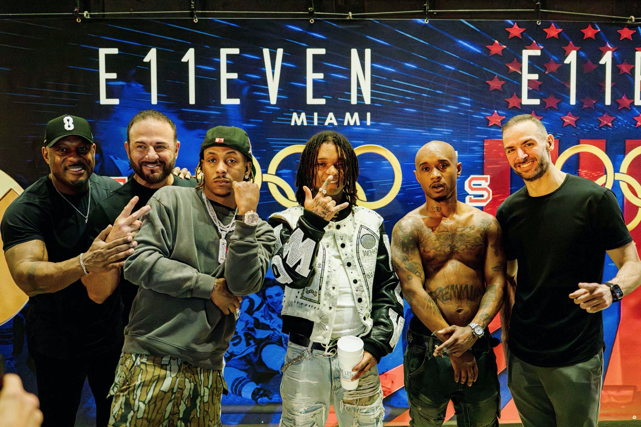photo of six men posing together in front of a step-and-repeat showing a logo for E11even Miami