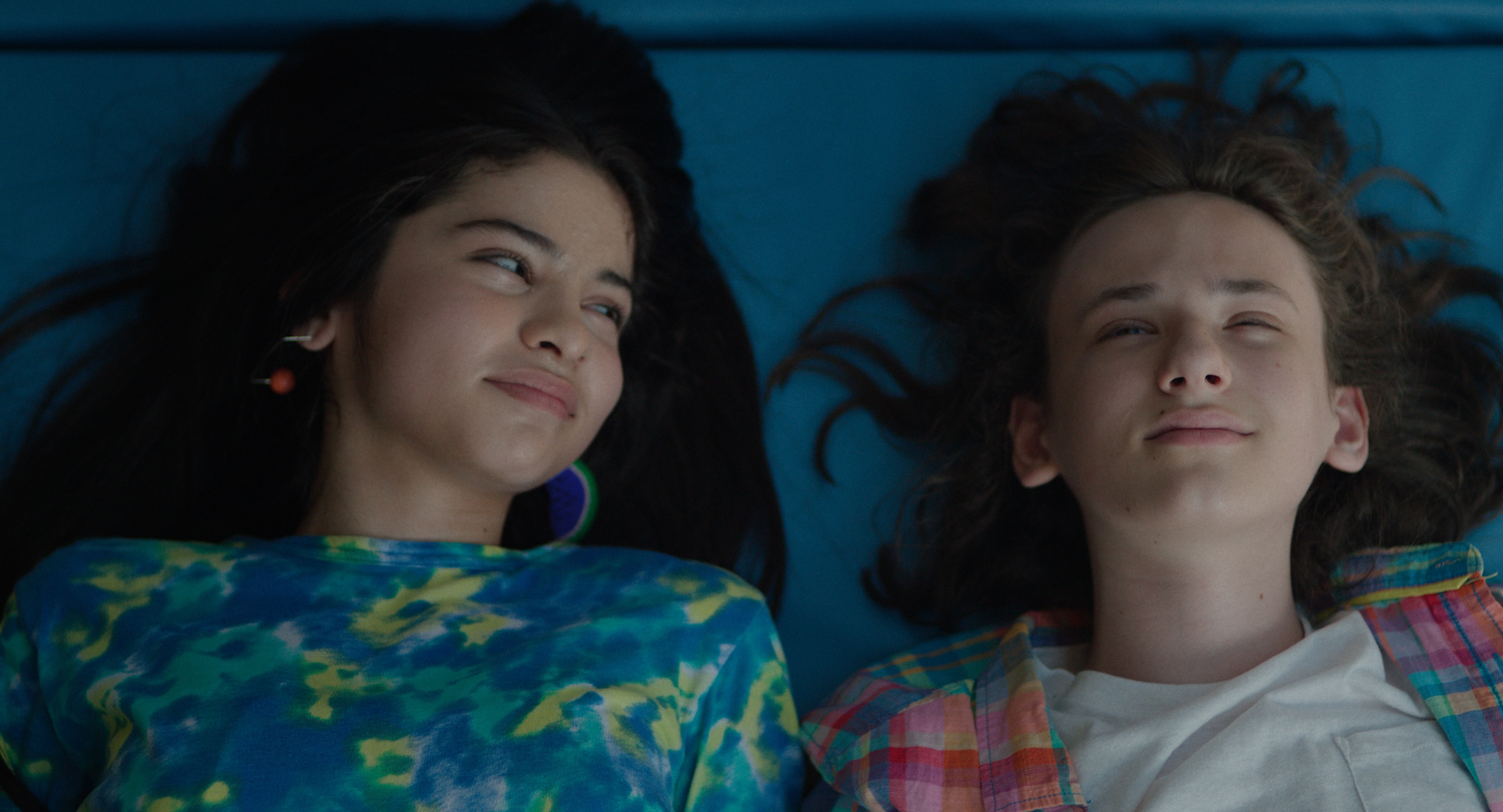 Still from the film 'Ethan Bloom' showing an overhead view of a young boy and older girl lying down. The boy looks up at the sky and the girl looks at the boy