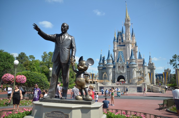 a statue of a man and Mickey Mouse stand before a castle