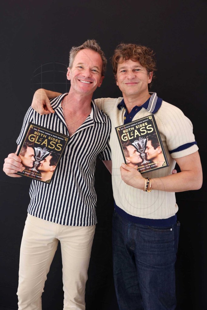 photo of Neil Patrick Harris and David Burtka posing together holding copies of books showing their faces with the title, "Both Sides of the Glass"
