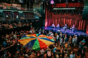 Photo of a concert with people holding a colorful fabric in the middle of the venue