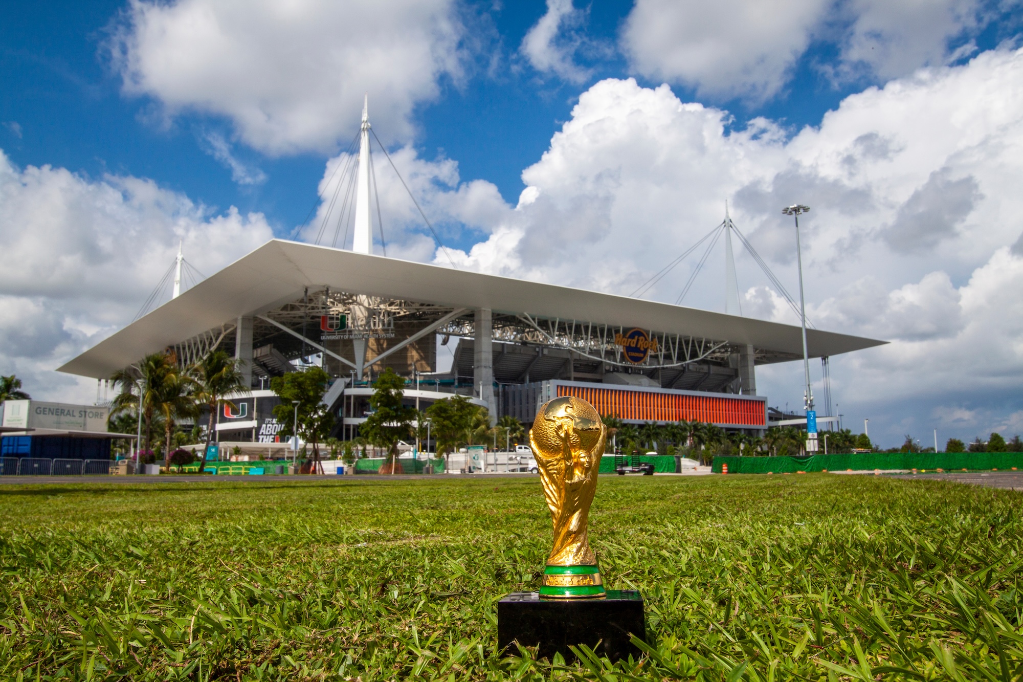 photo of the World Cup trophy on the grass in front of Miami's Hard Rock Stadium, which looms in the background