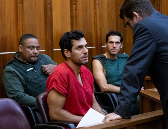 a deputy sits in a courtroom behind two men in shackles