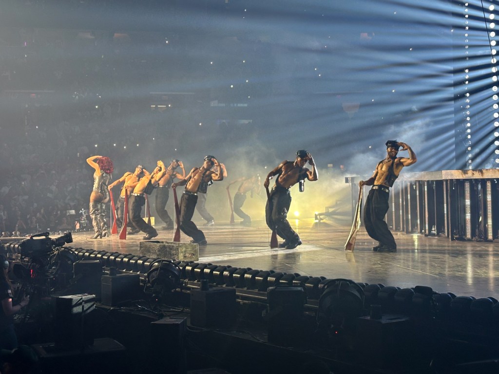 Photo of dancers on stage shirtless carrying toy riffles
