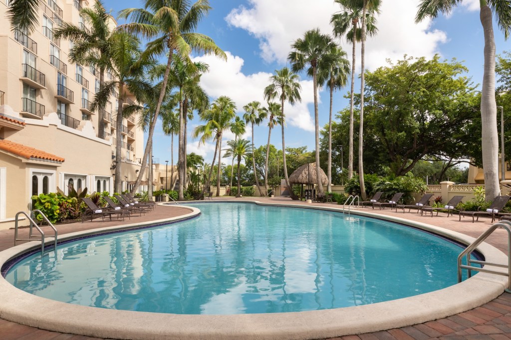 photo of a modest hotel pool surrounded by trees, the hotel building, and lounge chairs