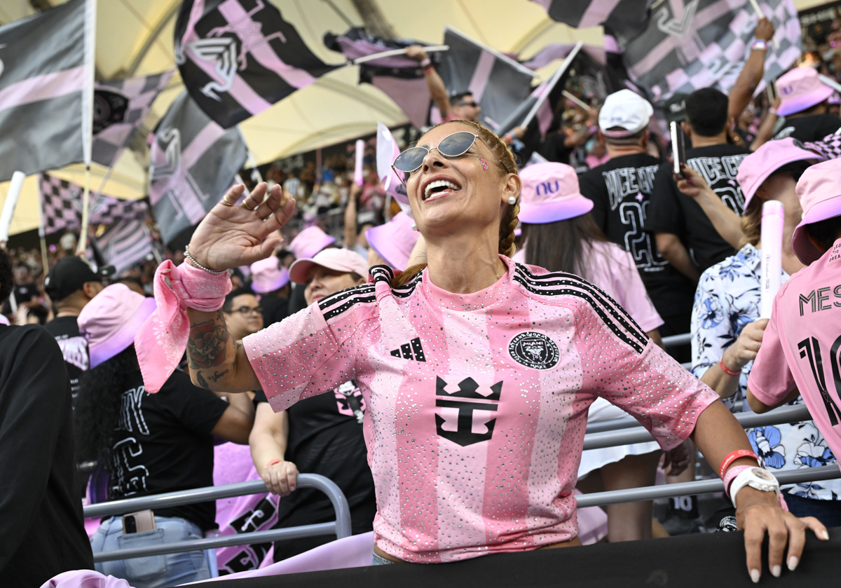 photo of a woman in a bedazzled Inter Miami FC shirt in the stands at a soccer game surrounded by a crowd of fans