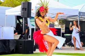 photo of a female Polynesian dancer in traditional dress dancing in front of festival tents