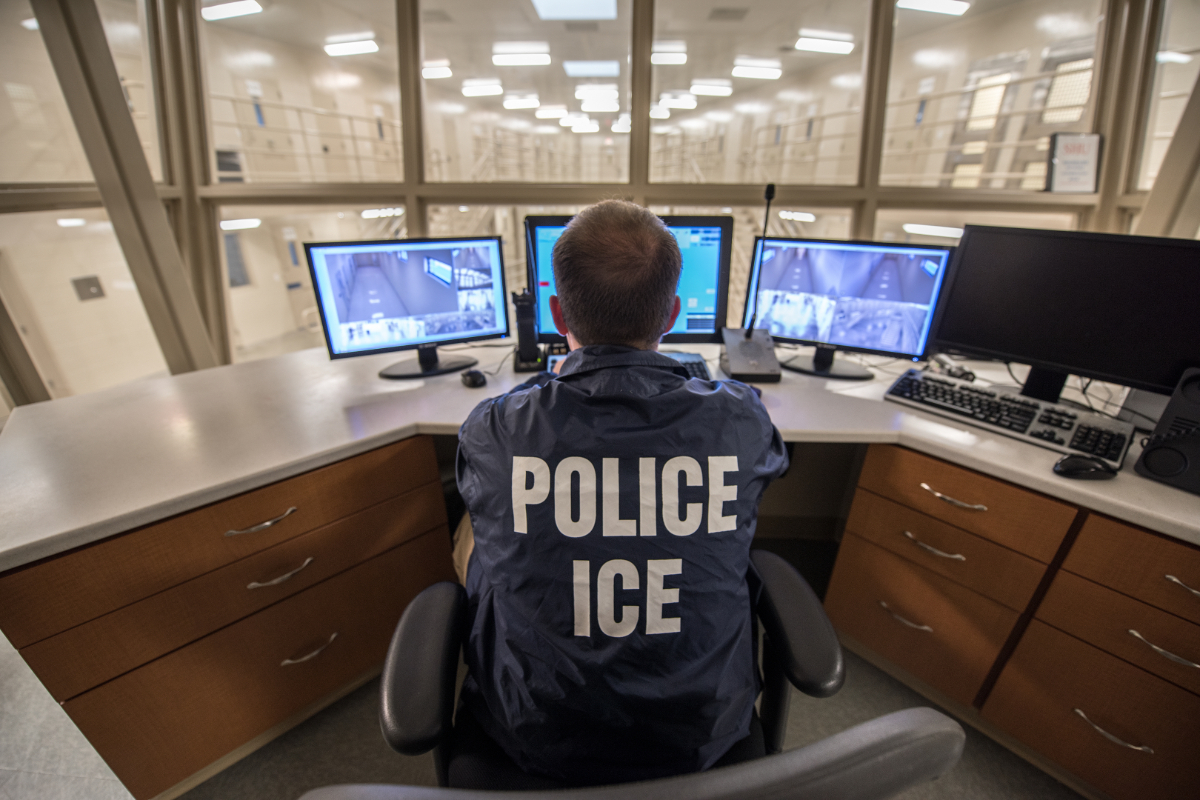 A photo of an ICE officer monitoring live video feed of a detention facility.