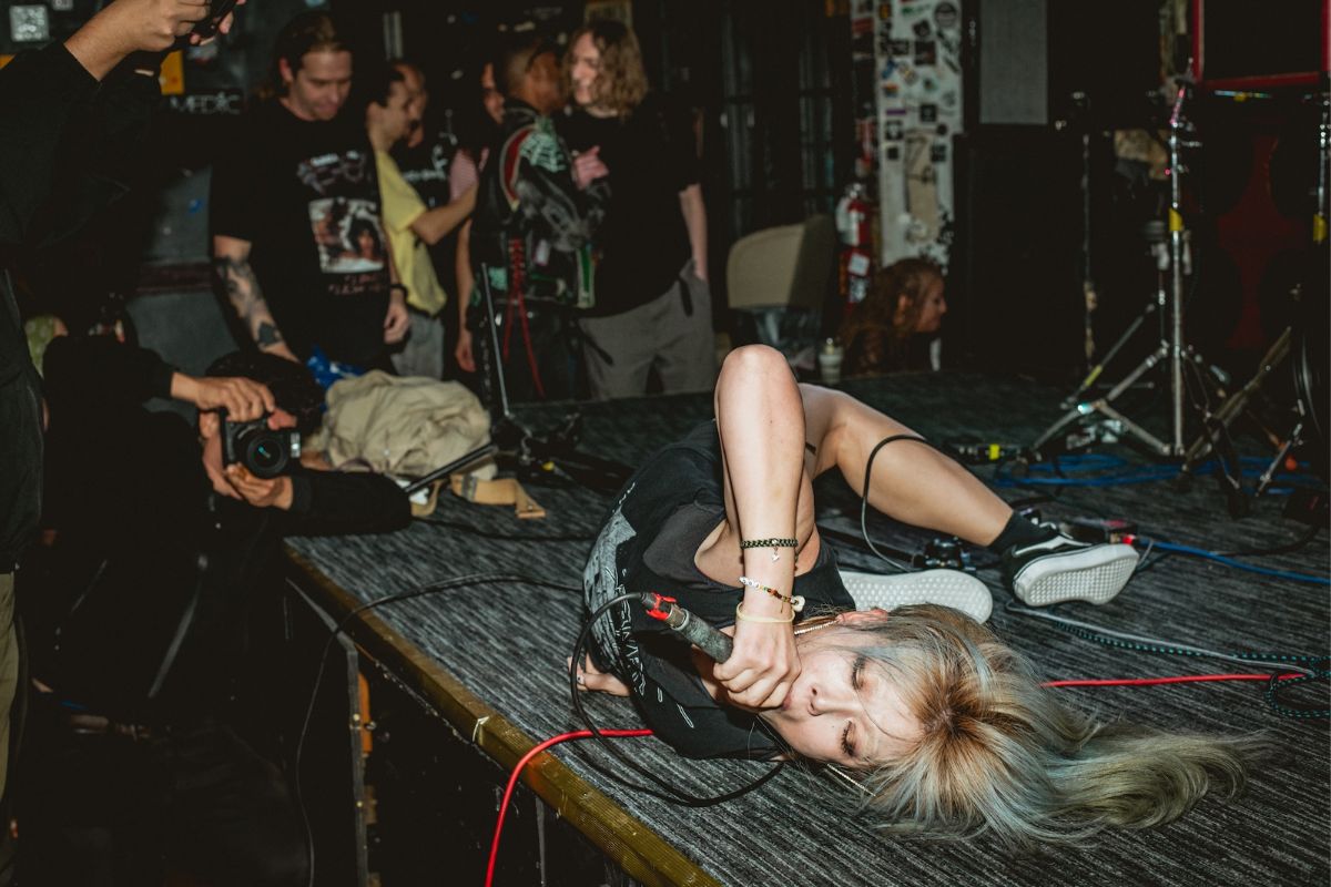 Photo of a woman singing on stage laying on the floor holding a microphone