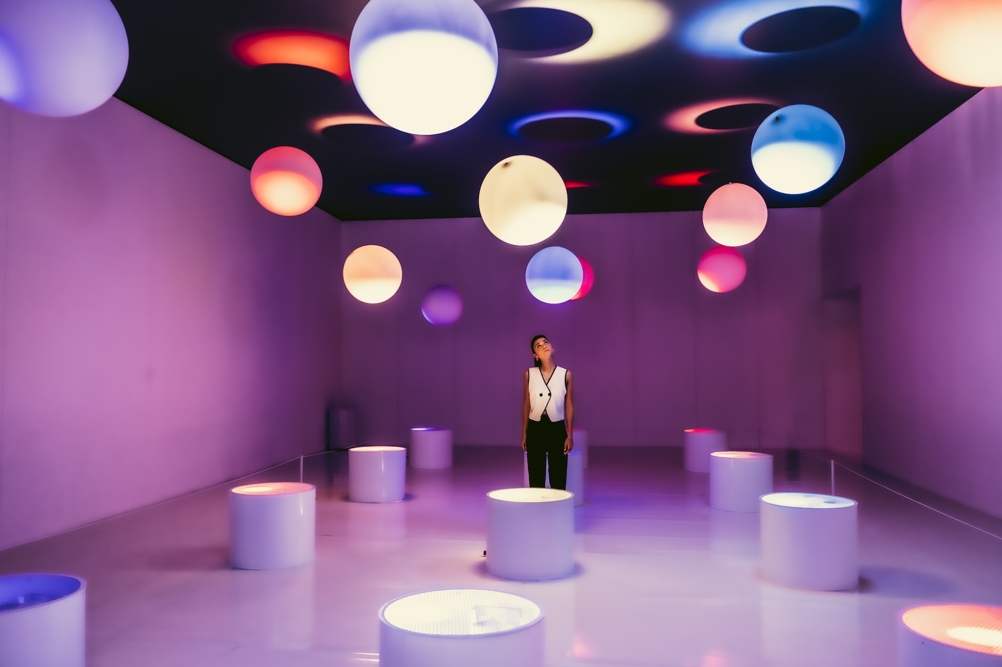 photo of a woman in a purple room inside a museum with different colored spheres on the roof and cylinders on the floor