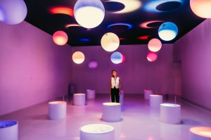 photo of a woman in a purple room inside a museum with different colored spheres on the roof and cylinders on the floor