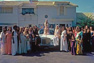 photo depicting a crowd of women around a Rolls-Royce. A woman sits on the car holding a poster depicting a cult leader