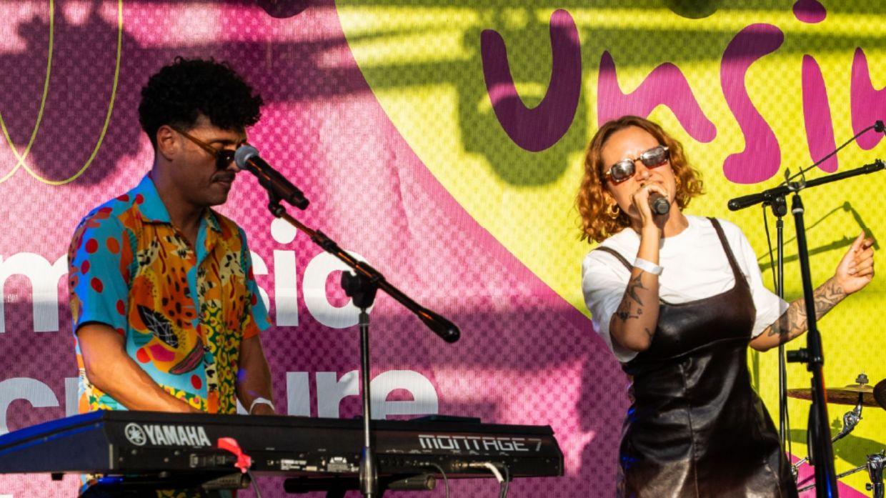 Photo of two musicians performing on stage in front of a sign that says Unsin.