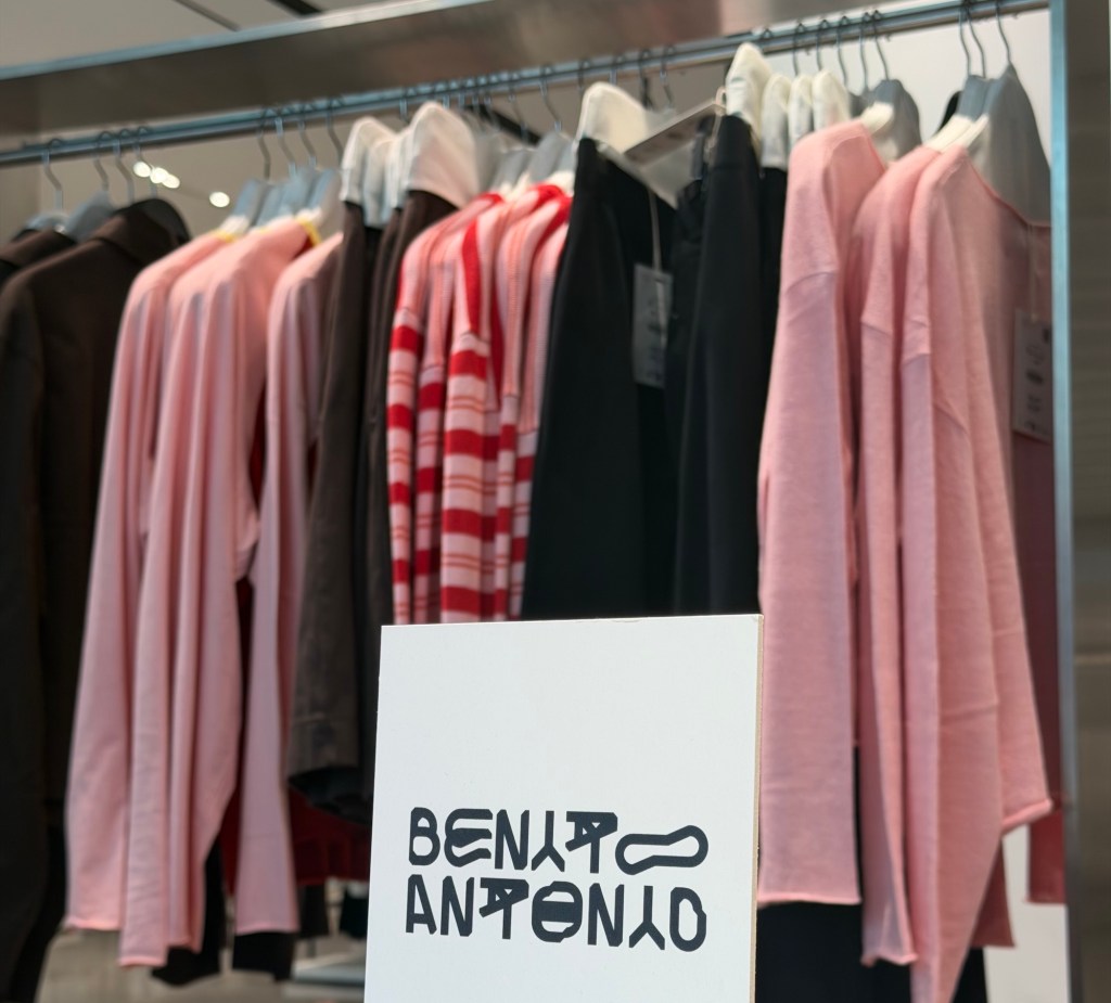 Photo of clothes on racks inside a store. A sign with the brand logo in the foreground reads, "Benito Antonio"