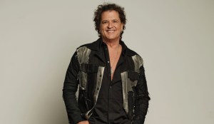 photo of singer Carlos Vives posing in a stylishly tattered blazer posing against a cream-colored backdrop