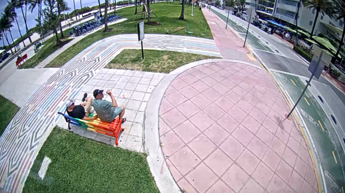 A screenshot from surveillance footage of two men sitting on a rainbow bench in Miami Beach.