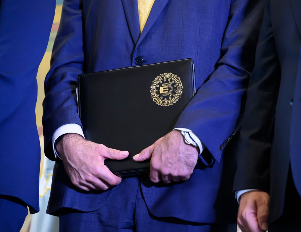 close-up photo of a man in a suit holding a folder with a government seal on it