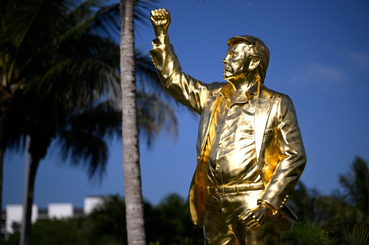 photo of a golden statue of Donald Trump with his fist in the air in front of an evening sky and palm trees