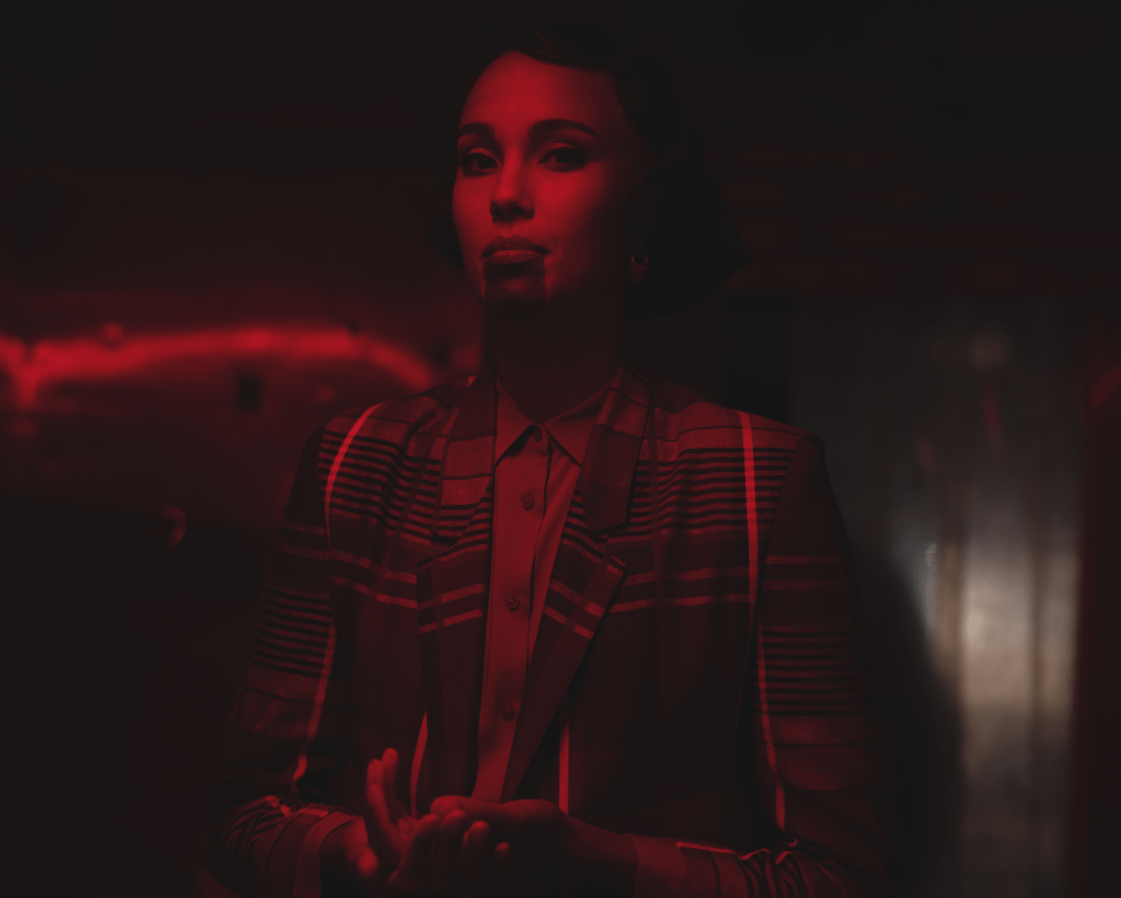 photo of a woman with a marking on her chin in a shirt and blazer looking at the camera while bathed in red light