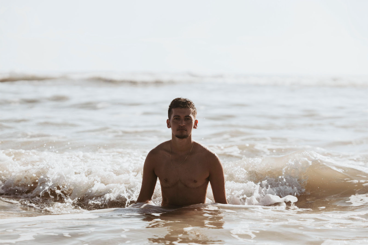 photo of a young man coming out of the ocean in daytime