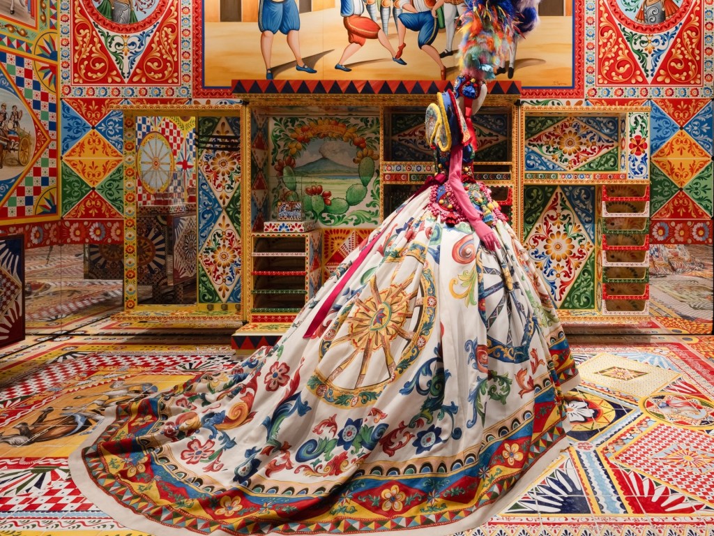 photo of an ornate Dolce&Gabbana dress on display inside a room with colorful painted tiles on the roof and walls
