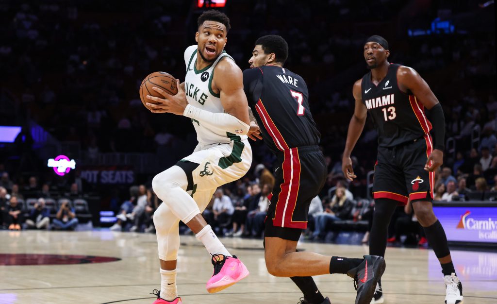 Giannis Antetokounmpo holds the basketball as he plays against two Miami Heat players on the basketball court