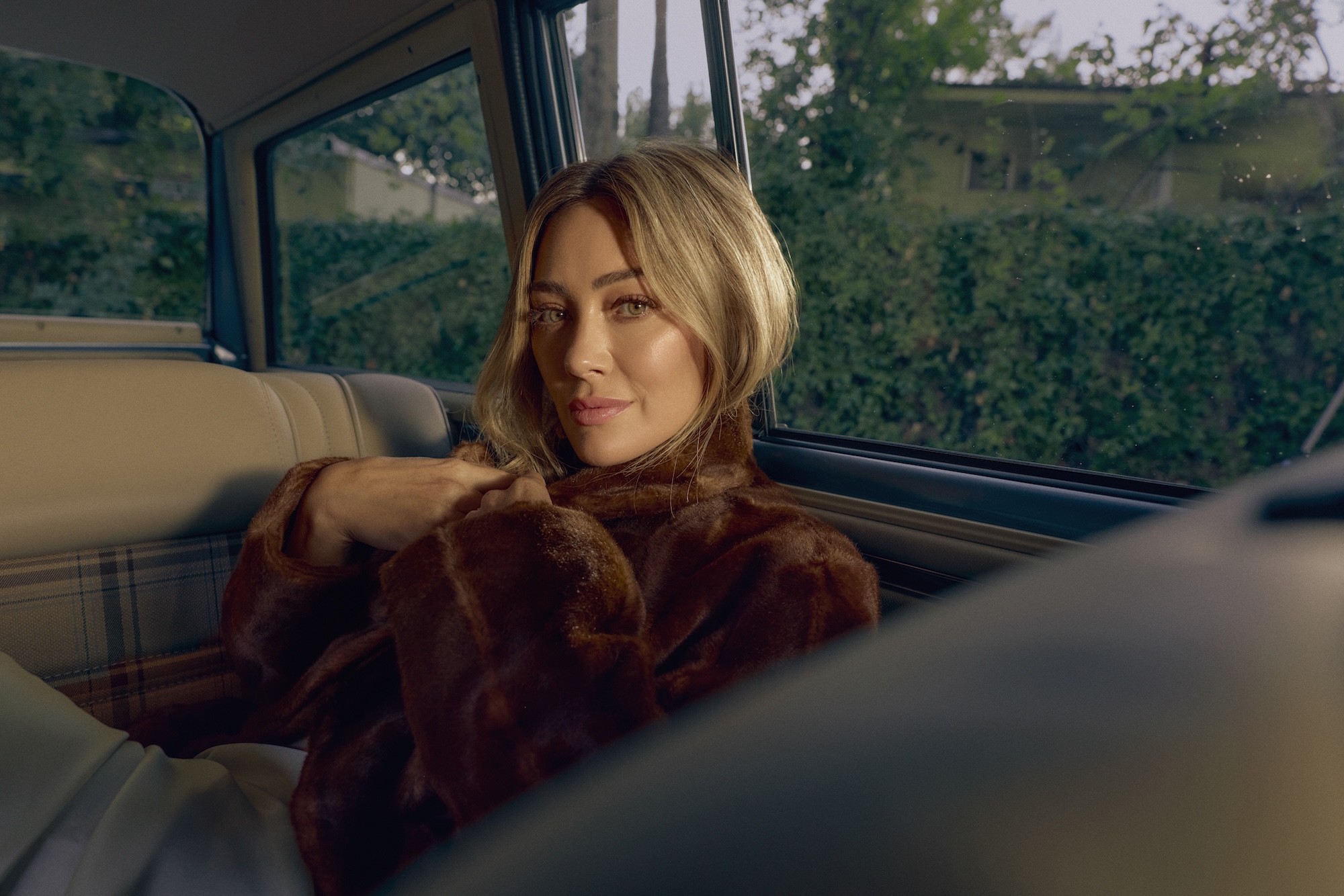 photo of singer Hilary Duff posing in a fur coat in the backseat of a car