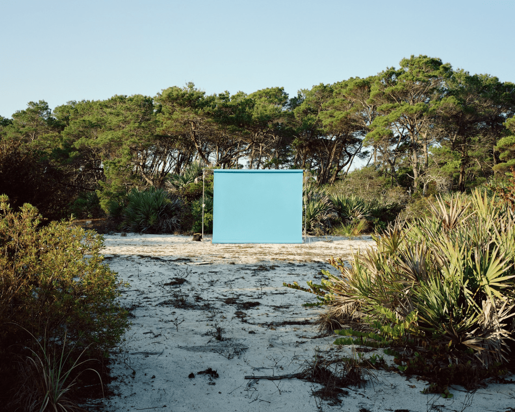 photo of a teal-blue photoshoot backdrop set up on the sand surrounded by trees