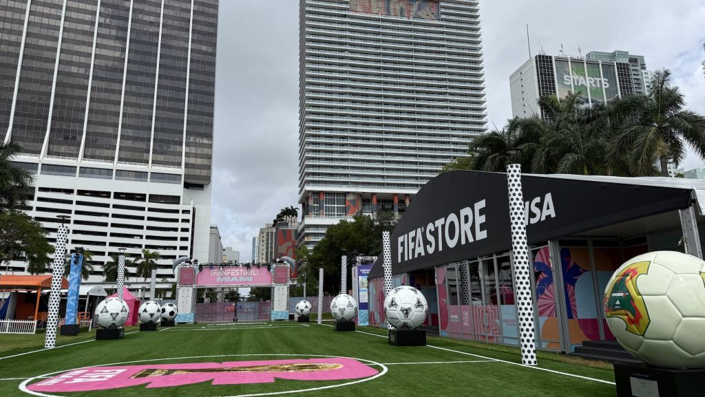 Photo of branded turf with skyscrapers in the background. A tent on right has a sign reading FIFA STORE