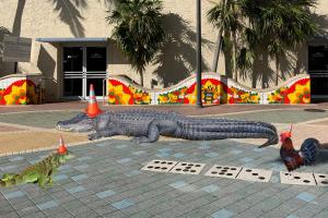 photoshopped image showing an iguana, alligator, and rooster with traffic cones on their heads in front of a mosaic mural on Miami's Calle Ocho