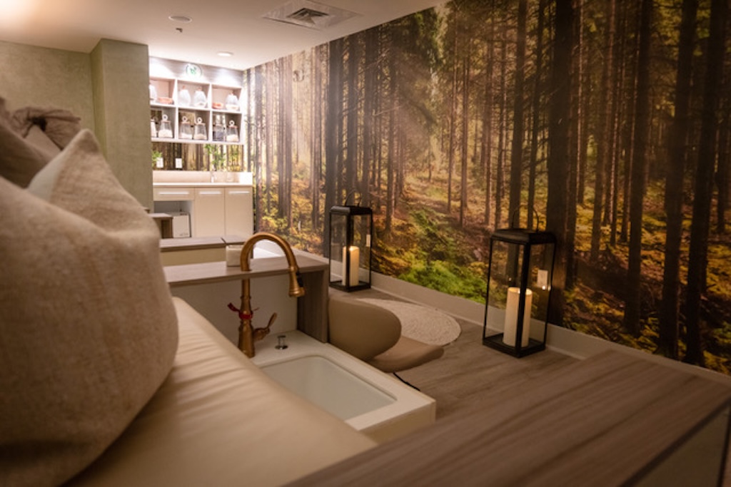 photo of a spa with a couch, sink, and wallpaper depicting a forest