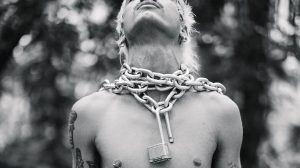 black-and-white photo of model Brian Linares posing with a thick metal chain and open lock around his neck